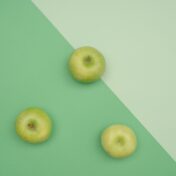 Three green apples on a dual-shade green background showcasing minimalist beauty and symmetry.